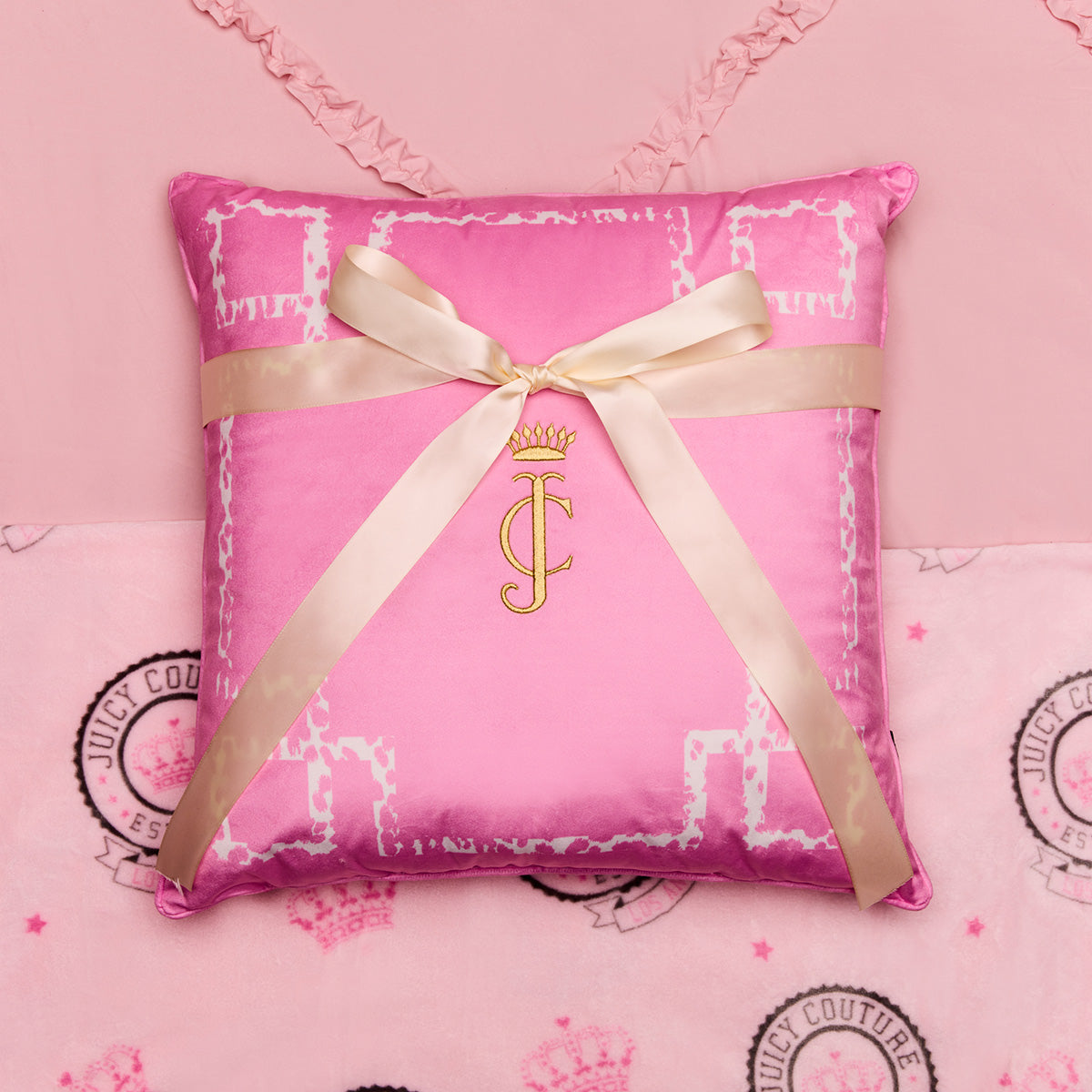 Pink pillow with a gold ribbon and logo on a pink background