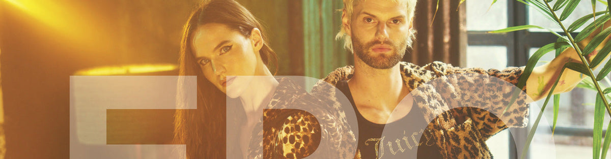 A man and a woman in leopard print jackets pose together behind large, semi-transparent letters.