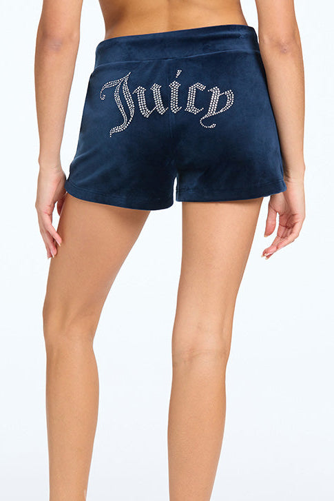 Someone adjusts the drawstrings of the Big Bling Velour Track Shorts, seen from the back in dark blue, featuring “Juicy” spelled out in rhinestones and stylish side pockets.
