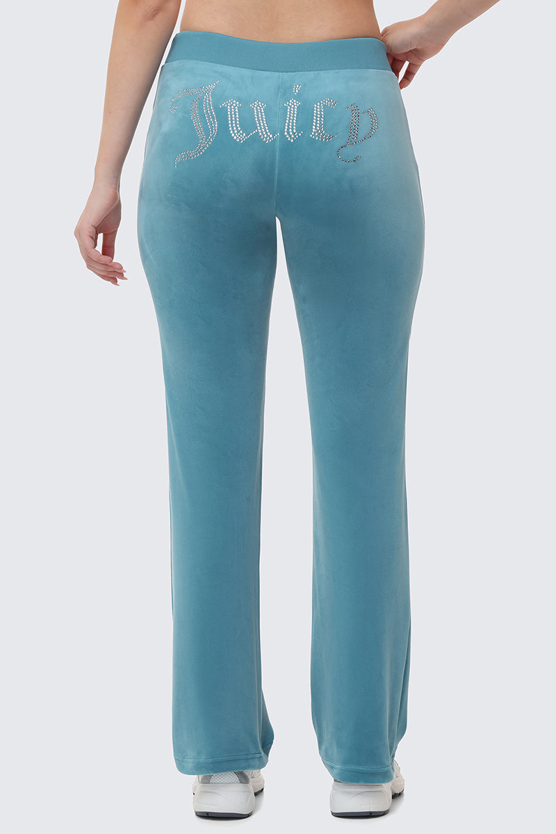 OG Big Bling Velour Track Pants in blue velour with the word Juicy spelled out in rhinestones across the back, capturing a classic Y2K aesthetic.