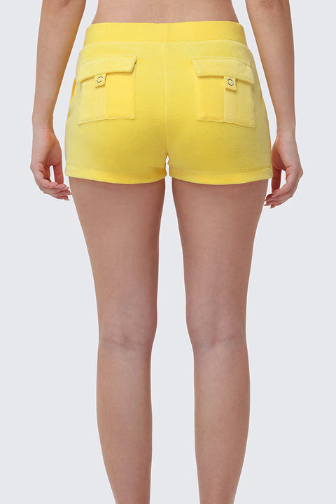 Someone stands against a plain light gray background, seen from the waist down and behind, wearing Heritage Cotton Velour Embroidered Shorts in bright yellow with back pockets.