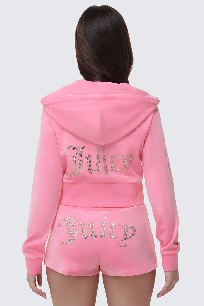 A woman is seen from the back wearing the Scottie Big Bling Velour Hoodie in pink with a zip front and matching shorts, both adorned with sparkling Juicy rhinestone logos.