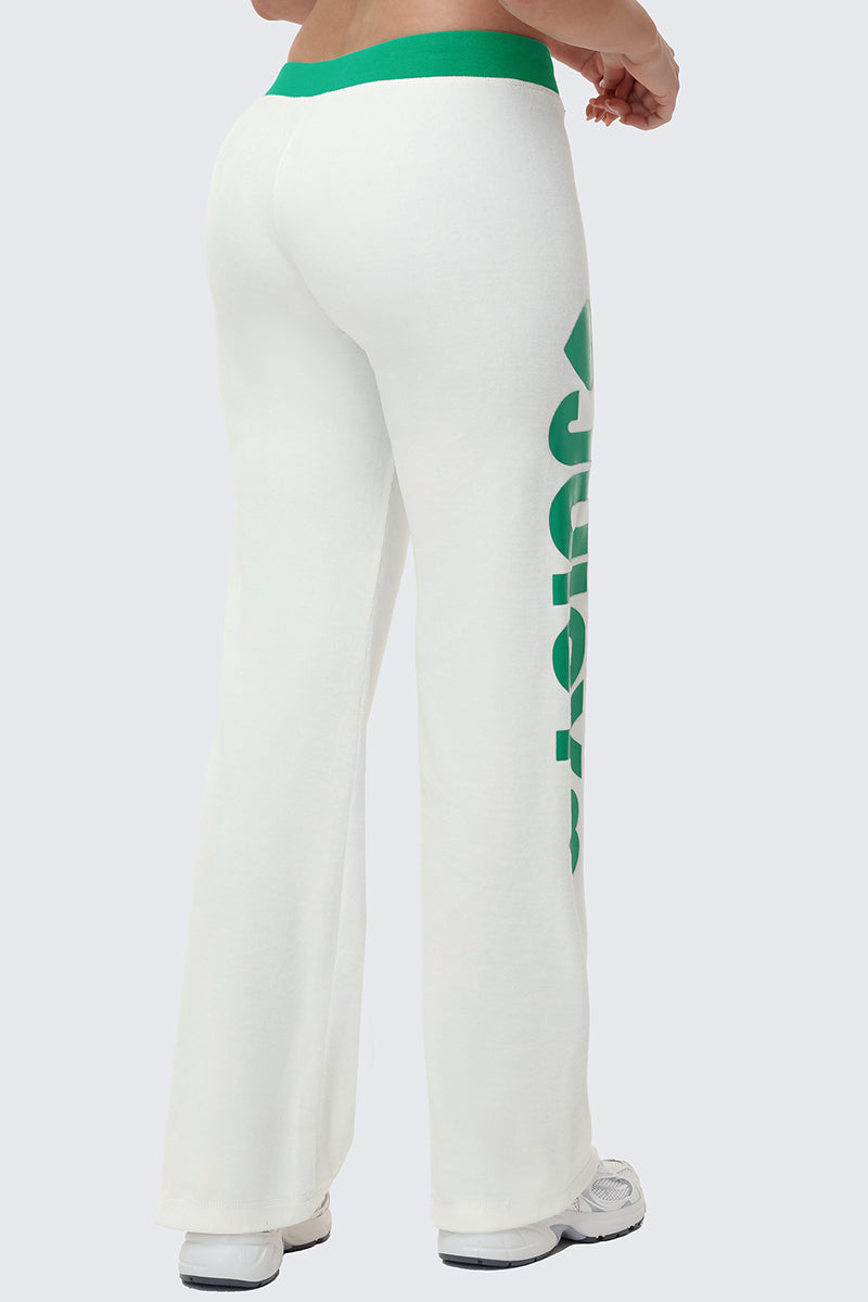 A person is seen from the back wearing Contrast Low Rise Track Pants—white flared sweatpants with a green waistband and green Juicy text down the left leg—teamed with white sneakers for a sporty lounge look.