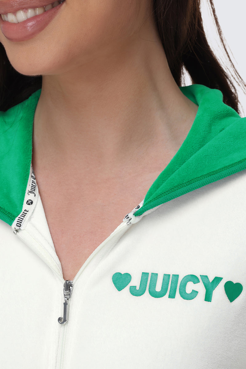Close-up of a woman smiling, wearing the Contrast Trim Logo Hoodie—a white zip hoodie with green hood, green heart logo, and "JUICY" on the chest. Only her lower face is visible.