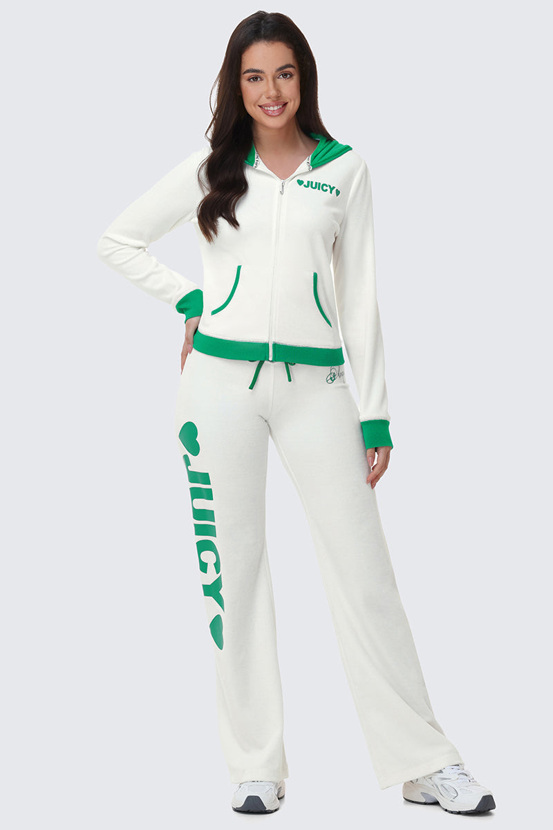 Woman smiling in a white Contrast Trim Logo Hoodie tracksuit with green accents. The zip-up hoodie features JUICY on the chest and a cozy hood, while matching pants display JUICY in green down the left leg. She stands hands on hips.