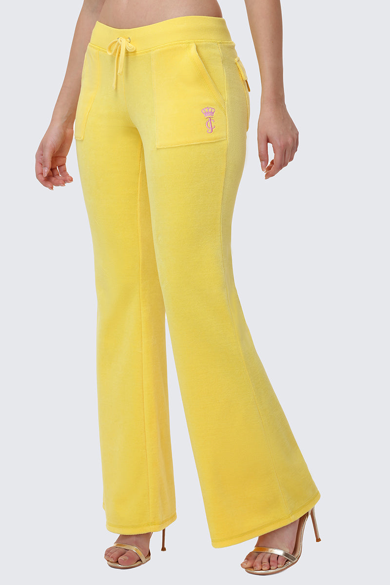Someone wears bright yellow Heritage Cotton Velour Track Pants with a high waist, front pockets, drawstring waist, and a small embroidered logo on the left pocket, paired with heels.