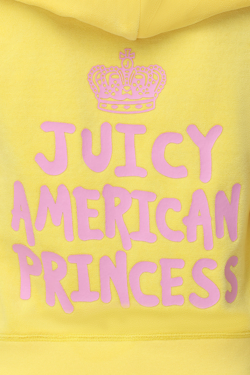The American Princess Heritage Hoodie is a yellow velour zip-up featuring "JUICY AMERICAN PRINCESS" in bold pink letters and a playful crown logo outlined in pink above the text.
