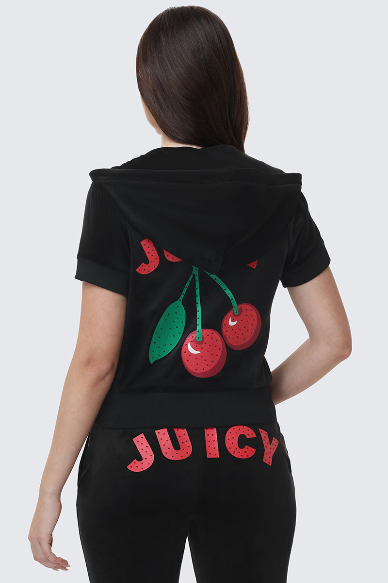A woman with long brown hair, seen from behind, wears the Cherry Bling Velour Hoodie with a Juicy cherry graphic and red "JUICY" text, paired with matching black pants featuring rhinestone-studded "JUICY" across the seat.