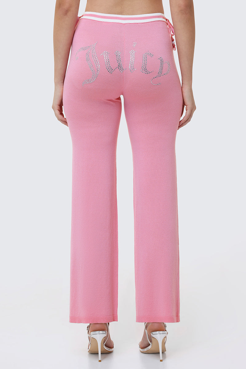 Someone is seen from behind wearing Big Bling Wide Leg Pants in pink velour with a rhinestone logo on the back, featuring a contrast striped waistband and paired with high-heeled sandals.