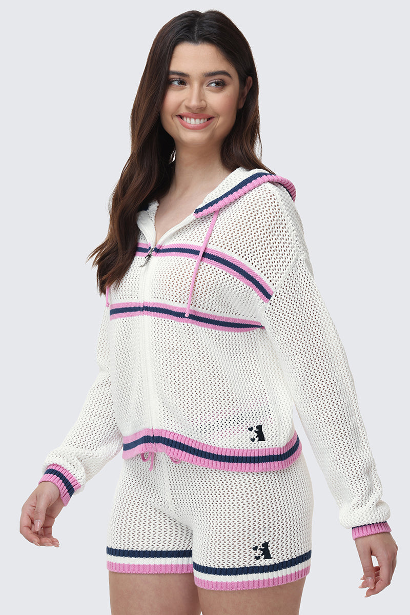 A woman smiles and looks to the side, wearing a Mesh Zip-Up Hoodie and matching shorts with pink, purple, and navy stripes. Both pieces feature a small black dog logo.