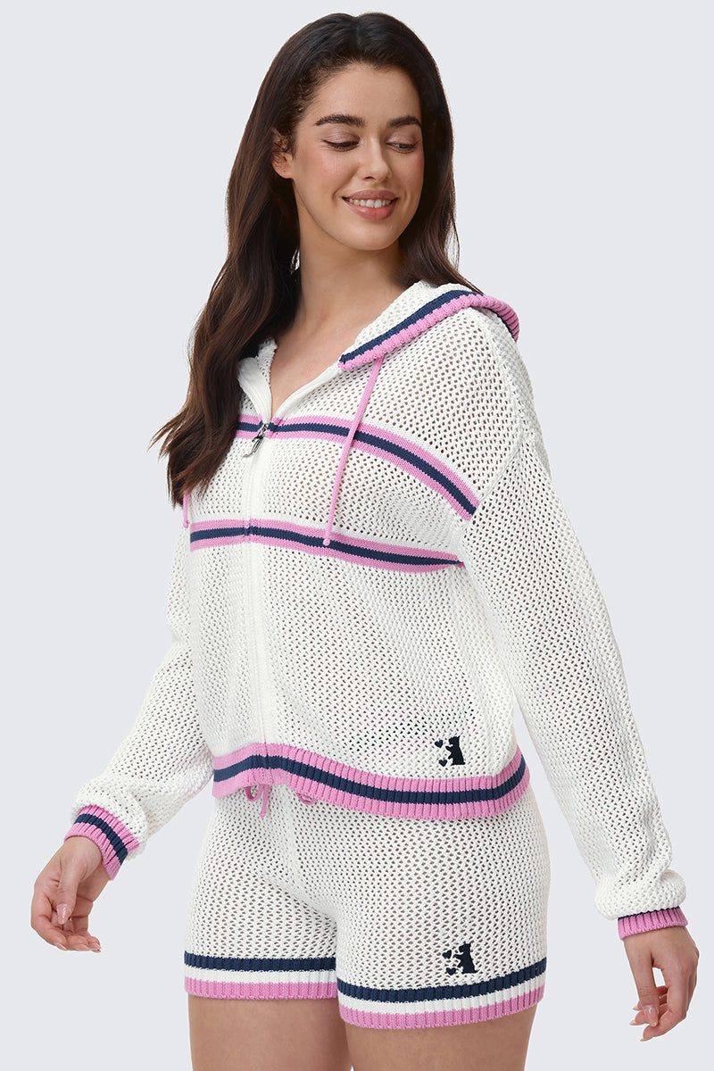 A woman smiles and looks to the side while wearing the Mesh Zip-Up Hoodie and matching shorts with pink and navy stripes. The white knit mesh hoodie has a zip-up front, and the shorts have a small bear logo.
