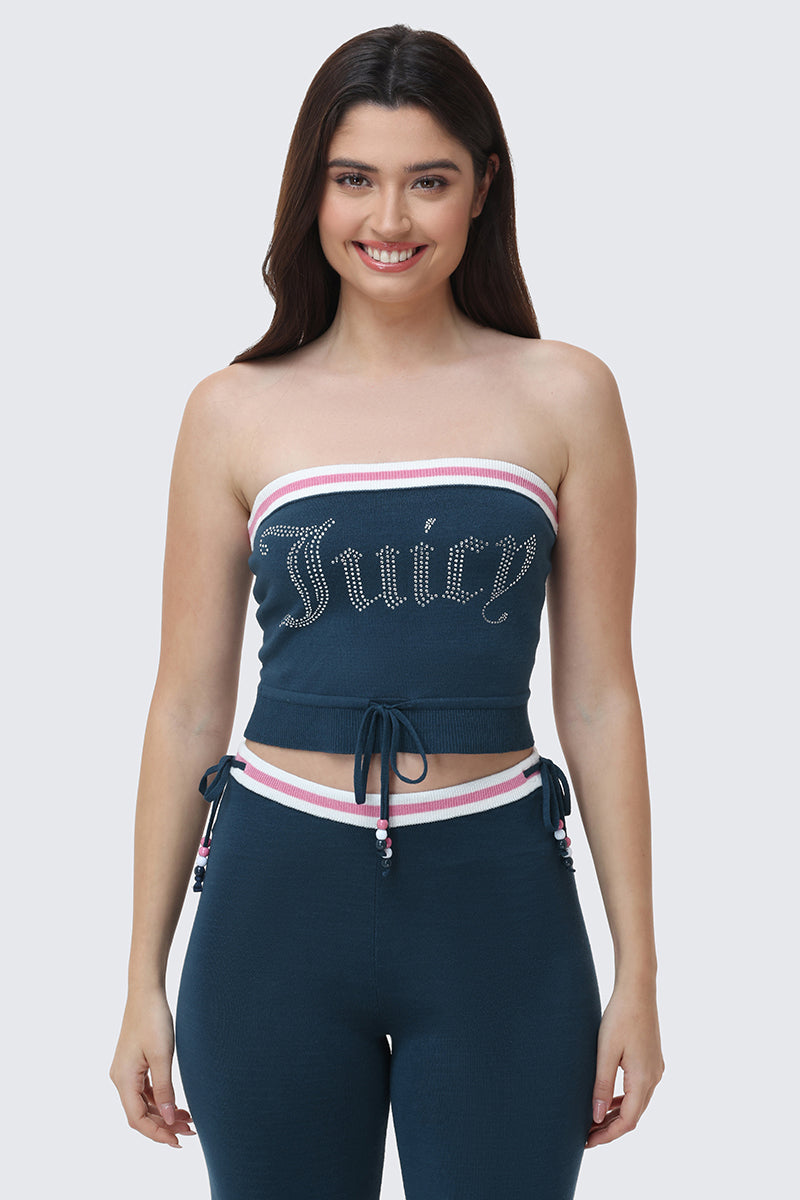 A woman with long brown hair smiles while wearing the Big Bling Tube Top in blue rhinestones and matching pants, both featuring white and pink trim plus drawstring details. The background is light gray.