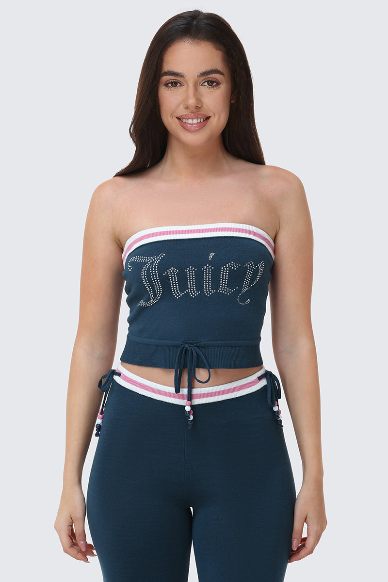 A woman with long dark hair wears the Big Bling Tube Top—strapless, blue, with "Juicy" in rhinestones—and matching blue pants featuring pink and white trim and drawstrings, standing against a plain light background.