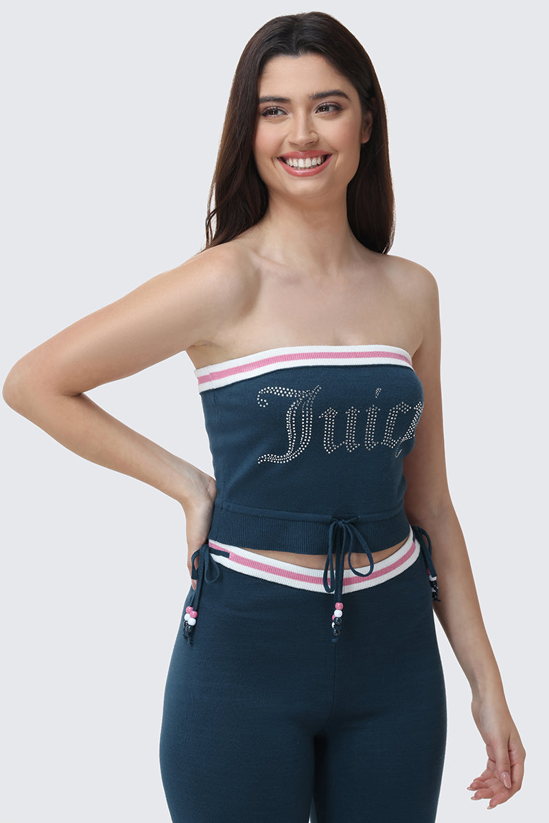 A woman smiles while wearing the Big Bling Tube Top, a strapless blue top with "Juicy" on it, paired with matching blue pants featuring white and pink striped trim and drawstrings.