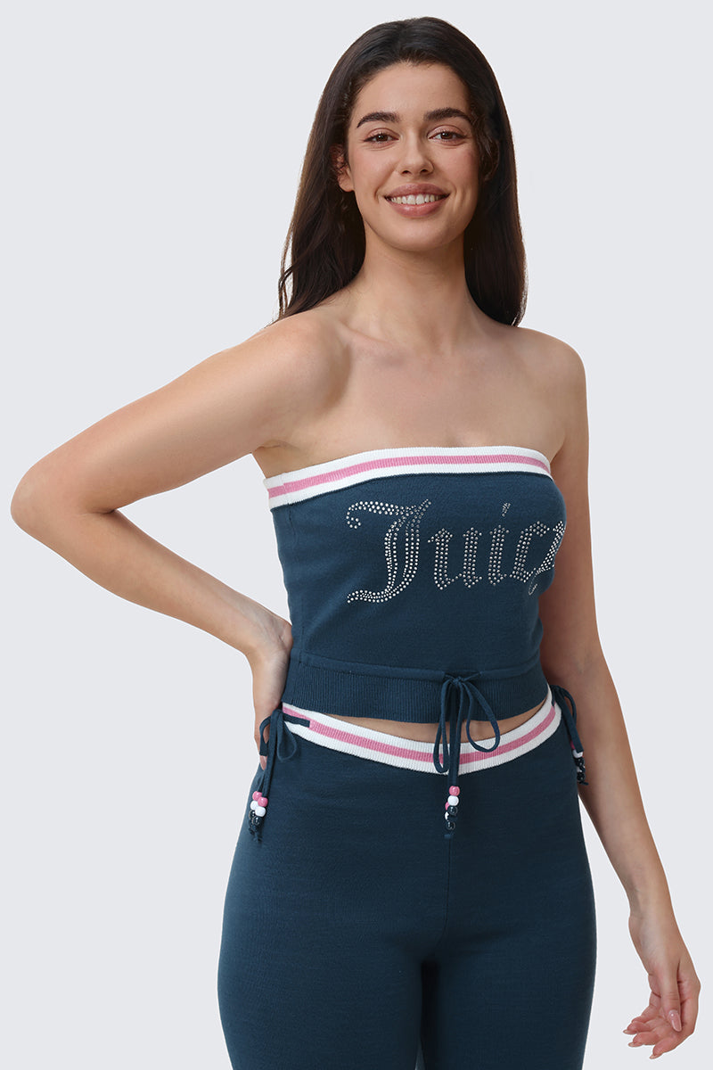 A woman with long brown hair smiles while wearing the Big Bling Tube Top in blue, featuring rhinestone "Juicy" lettering, paired with matching blue pants accented with white and pink trim and drawstrings.