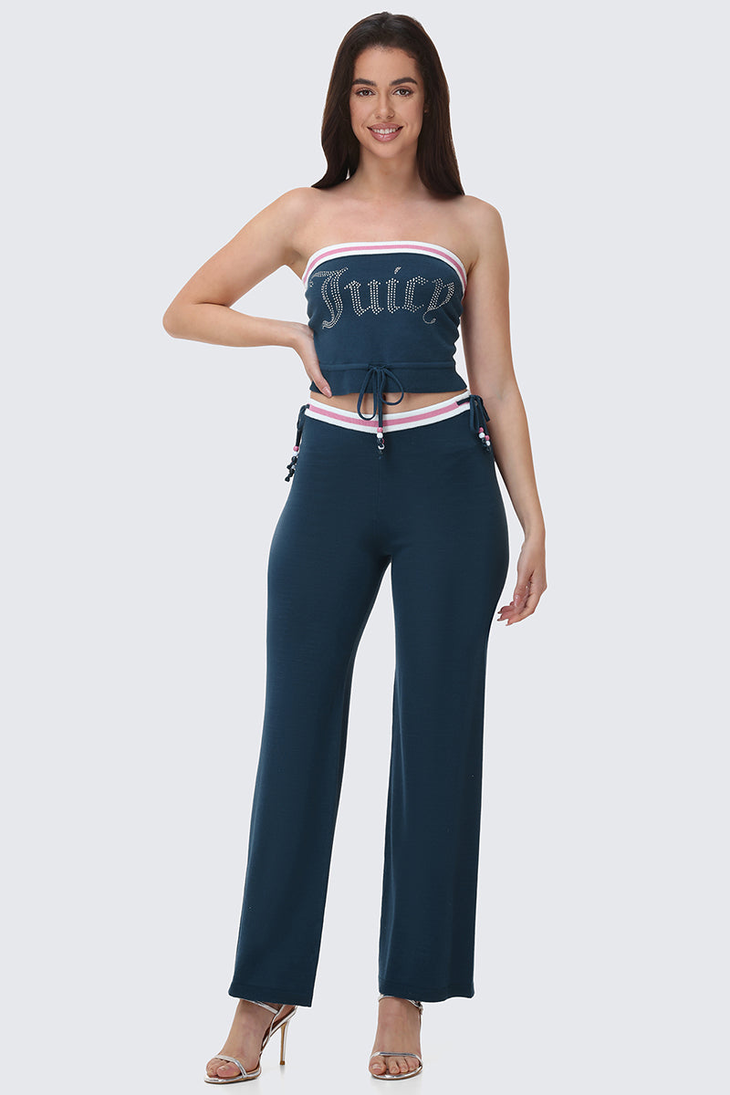 A woman stands against a plain light background, smiling with one hand on her hip, wearing the Big Bling Tube Top in dark blue and matching wide-leg pants.