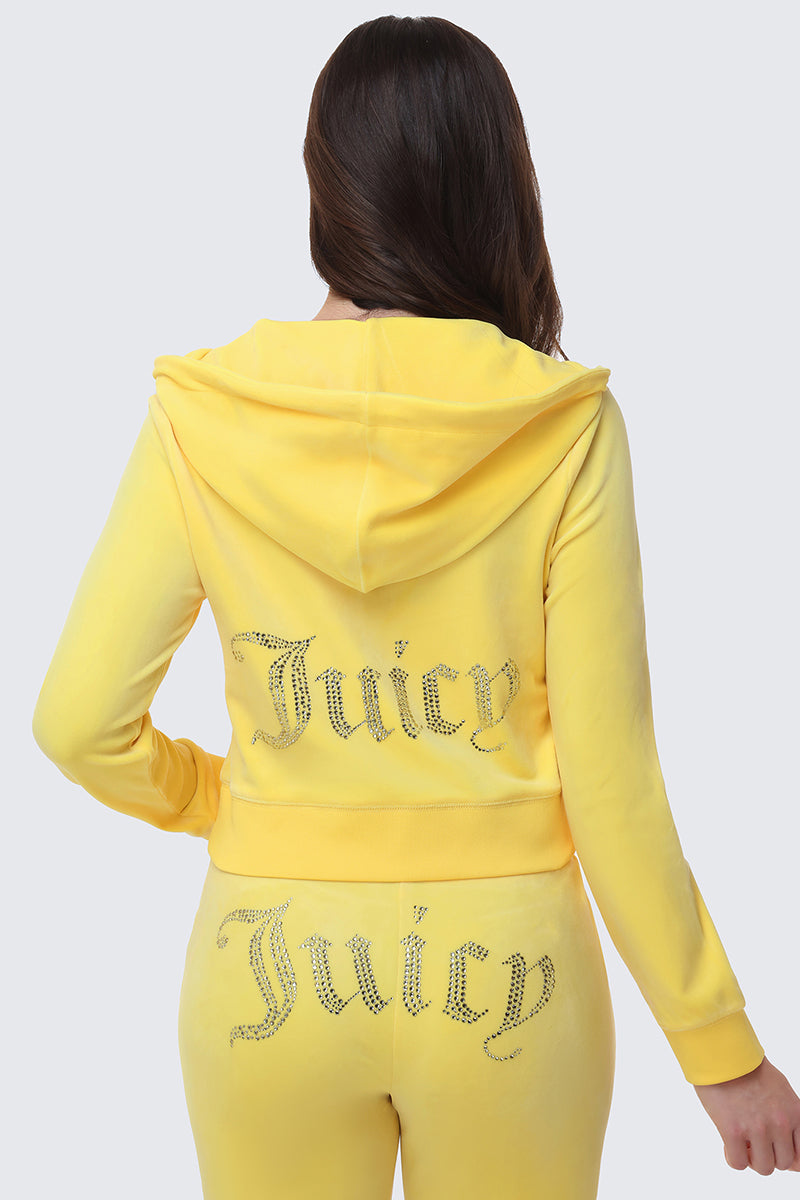 A woman with long brown hair, hood down, faces away wearing the OG Big Bling Velour Hoodie in yellow with rhinestone Juicy embellishments on the back of the jacket and seat of the pants.
