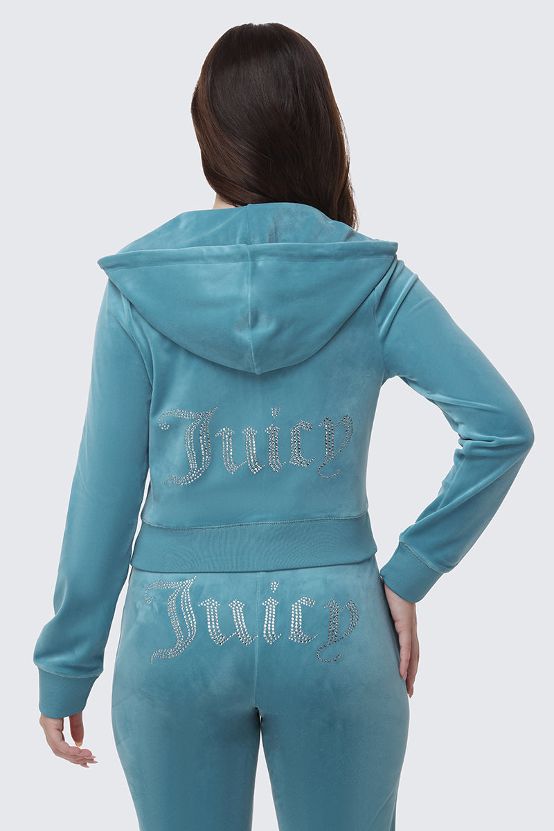 A person with long brown hair, seen from behind, wears the OG Big Bling Velour Hoodie—a teal Juicy tracksuit featuring rhinestone Juicy branding on the soft, comfy jacket and pants for a luxe, stylish look.