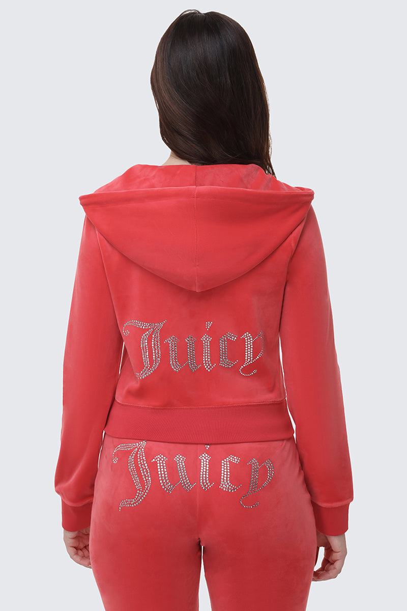 A person with long brown hair, seen from the back, wears a pink OG Big Bling Velour Hoodie and matching pants, both featuring bold rhinestone Juicy embellishments for a luxe twist.