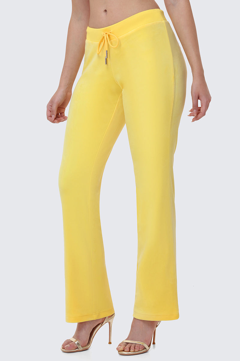 A person models the OG Big Bling Velour Track Pants in bright yellow with Juicy embellishment, paired with open-toe high heels, against a plain light background. Only the lower body is visible.