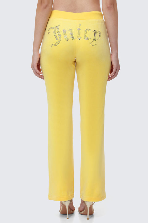 A woman shows off Y2K style in OG Big Bling Velour Track Pants with “Juicy” in rhinestones on the back, posing with her back to the camera and pairing the look with high-heeled sandals.
