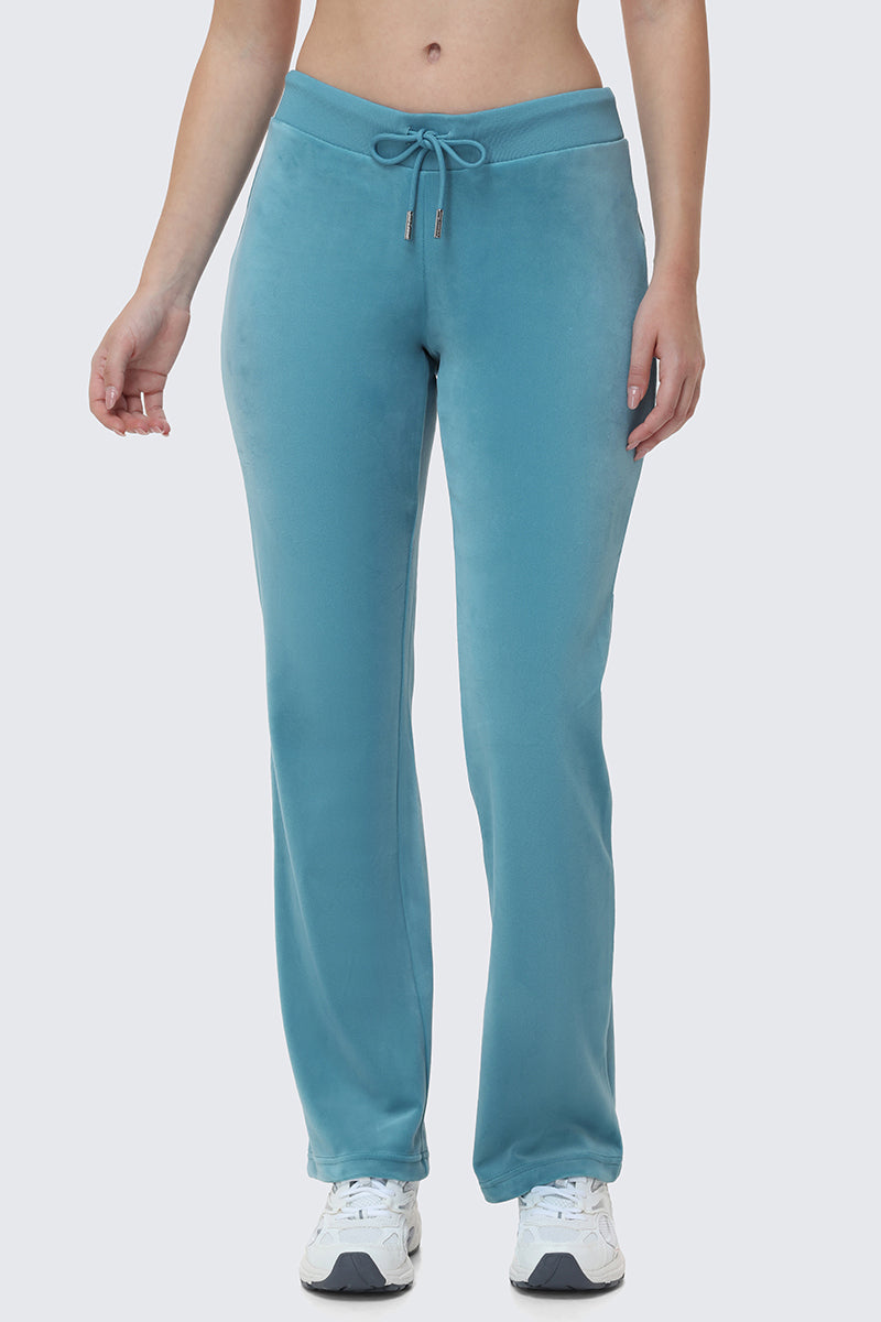 A person wears OG Big Bling Velour Track Pants in light blue with white sneakers, shown waist down against a plain light background.