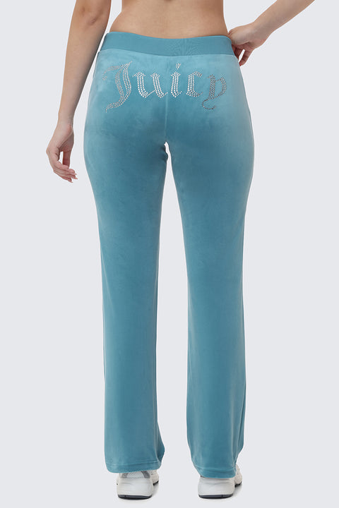 Someone wearing OG Big Bling Velour Track Pants in light blue, featuring "Juicy" spelled in rhinestones across the back, stands with their back to the camera in a Y2K-inspired look.