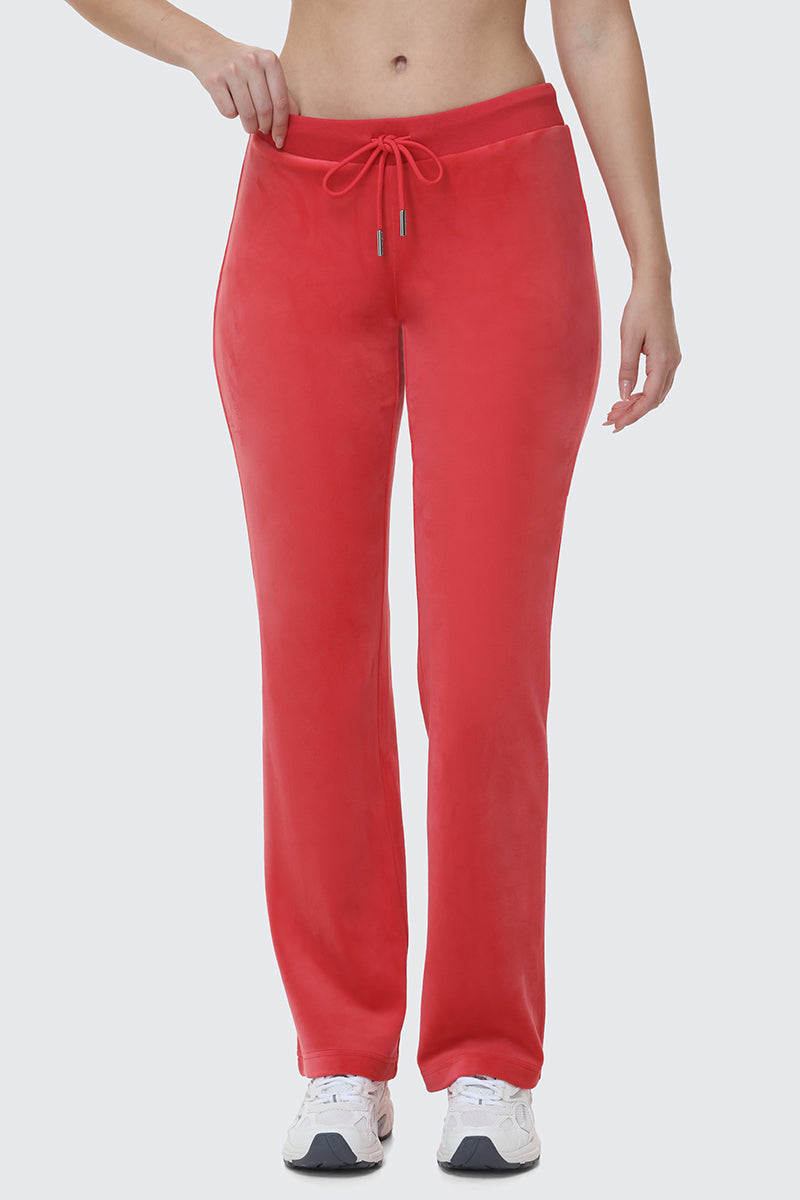 A person in bright red OG Big Bling Velour Track Pants and white sneakers stands against a plain light background, channeling iconic Y2K style with a partially visible upper body.