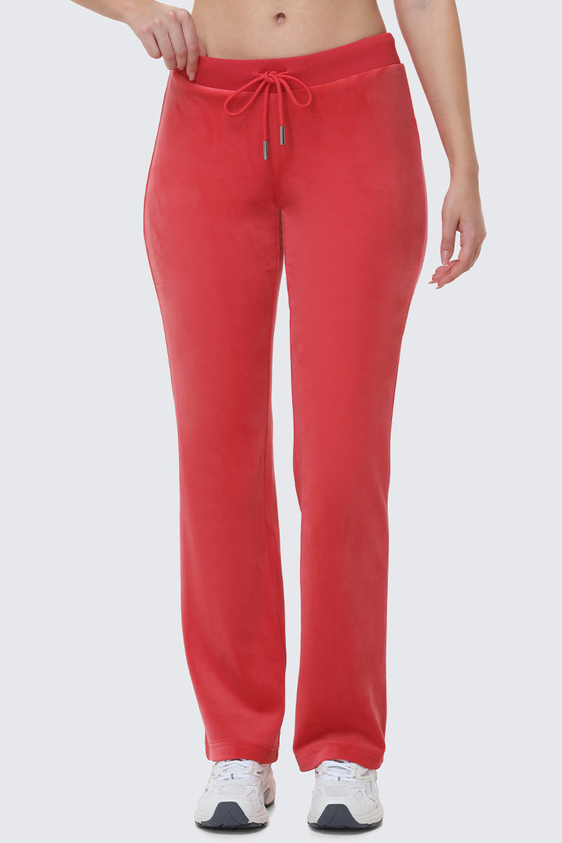 Wearing OG Big Bling Velour Track Pants in bright red, styled with a drawstring waist and paired with white sneakers, a person poses against a plain light background, visible only from the shoulders down.