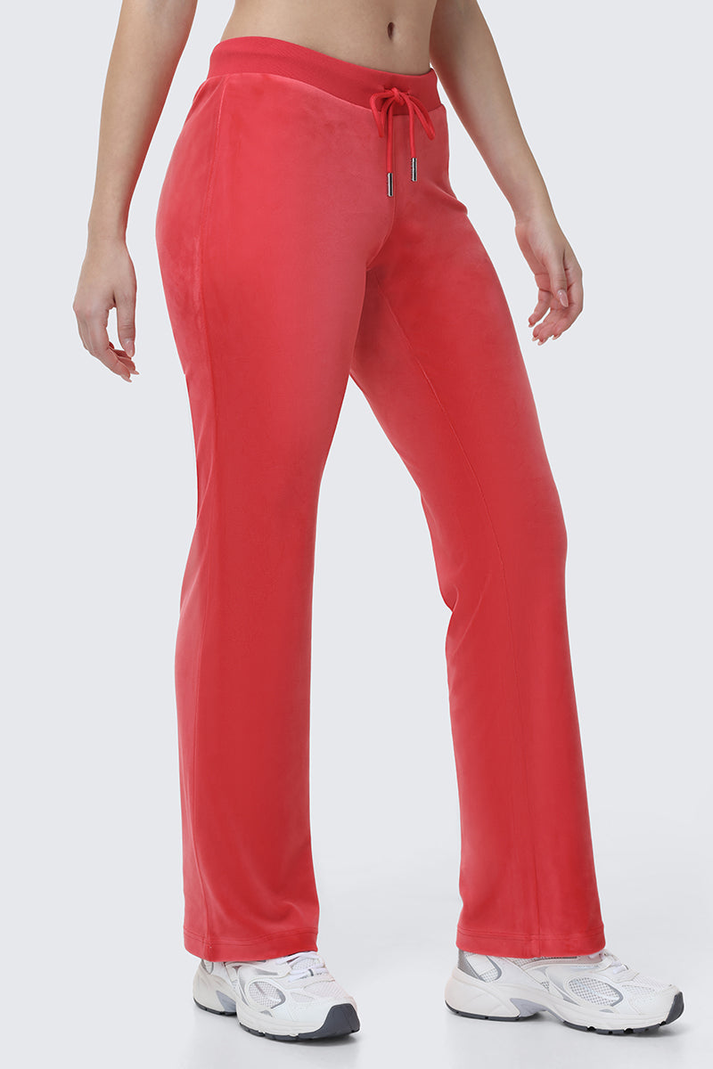 A person wearing OG Big Bling Velour Track Pants in bright red with flared legs and a drawstring waist, paired with white sneakers, stands against a plain light background.