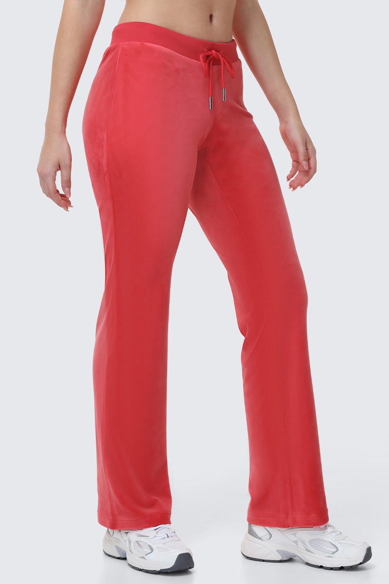 A person wears OG Big Bling Velour Track Pants in bright red with a drawstring and white sneakers, standing against a plain light background. The photo highlights the retro Y2K style by focusing on the lower torso and legs.