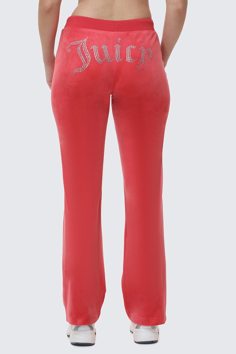 A person stands in iconic Y2K style, wearing OG Big Bling Velour Track Pants in bright pink with rhinestones across the back and white sneakers, shown from behind.