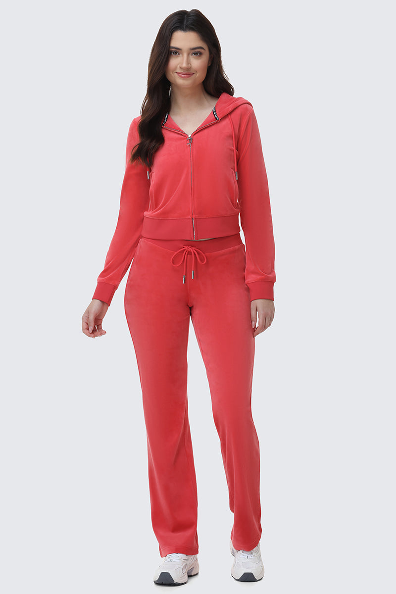 A woman wears OG Big Bling Velour Track Pants in bright pink with a matching zip-up hoodie and white sneakers, embodying classic Y2K style against a plain light gray background.