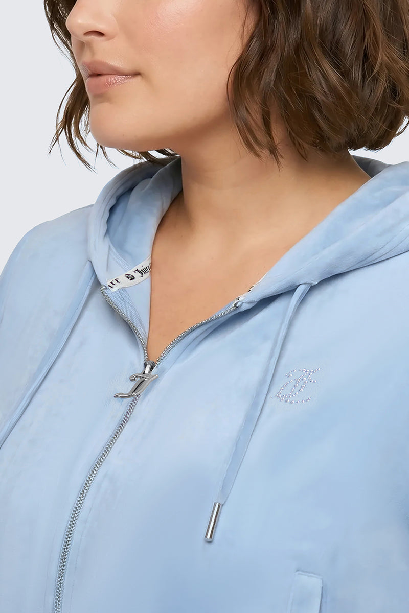 A woman with short brown hair models the Plus-Size OG Big Bling Velour Hoodie in light blue, featuring silver-tipped drawstrings. Only her lower face and upper torso are visible.