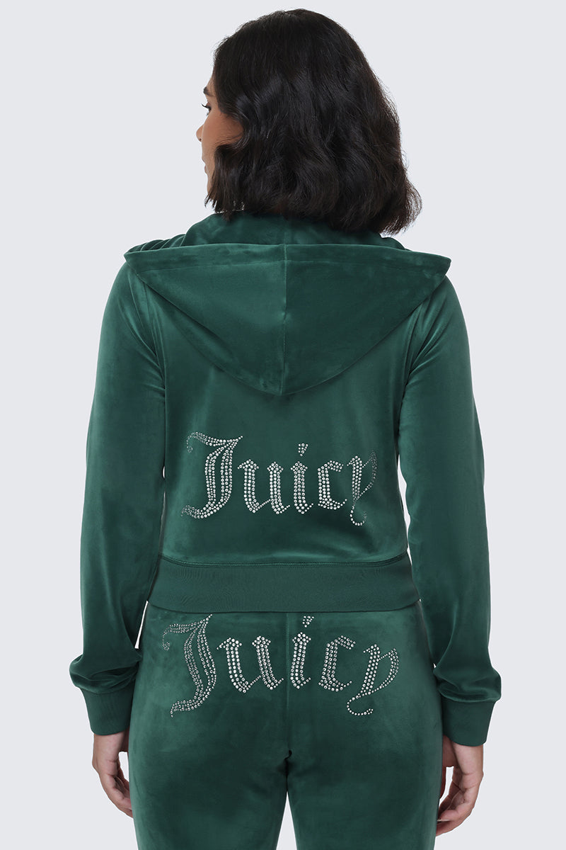 A woman with shoulder-length dark hair is seen from behind wearing the OG Big Bling Velour Hoodie in green, its back adorned with a rhinestone Juicy logo that perfectly channels the iconic Y2K vibe.