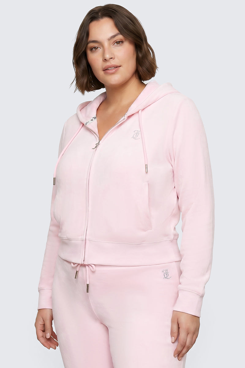 A woman with short brown hair models the Plus-Size OG Big Bling Velour Hoodie in light pink, embellished with rhinestones and paired with matching sweatpants, standing against a plain light gray background for an effortlessly cool Y2K-inspired look.