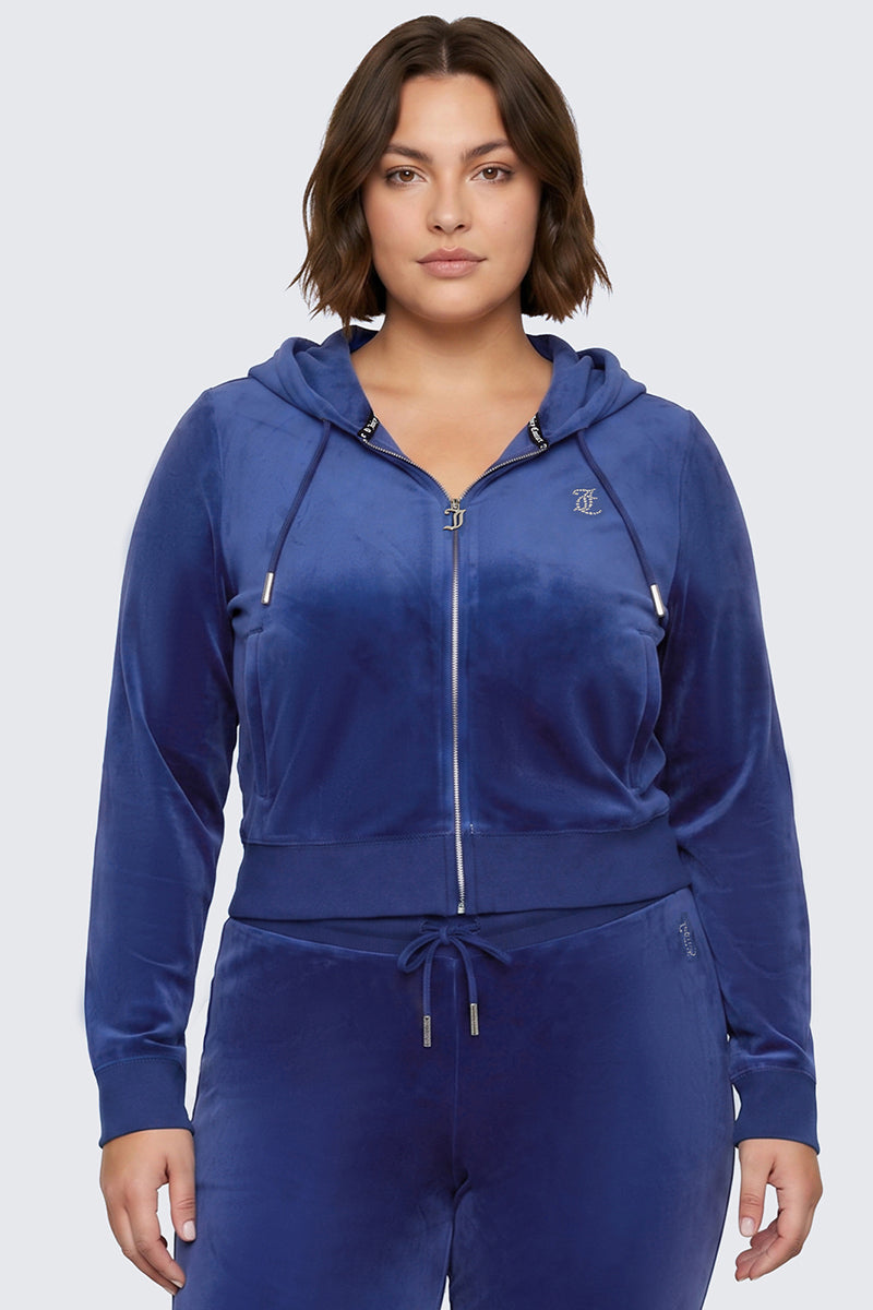 A woman wearing the Plus-Size OG Big Bling Velour Hoodie in royal blue, featuring a rhinestone Juicy logo and matching drawstring pants, stands facing forward against a plain light gray background, channeling classic Y2K style.