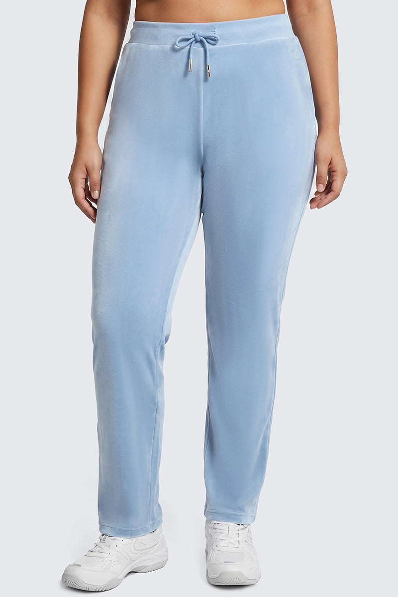 Wearing the Plus-Size OG Big Bling Velour Track Pants in light blue, complete with a drawstring waist, and pairing them with white sneakers, this person channels Y2K style while standing against a simple, light background.