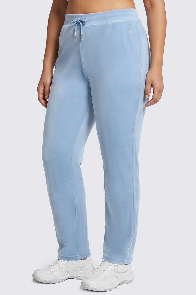 A person wearing Plus-Size OG Big Bling Velour Track Pants in light blue with subtle Y2K vibes and white sneakers stands against a plain background, with only the lower half of the body visible.
