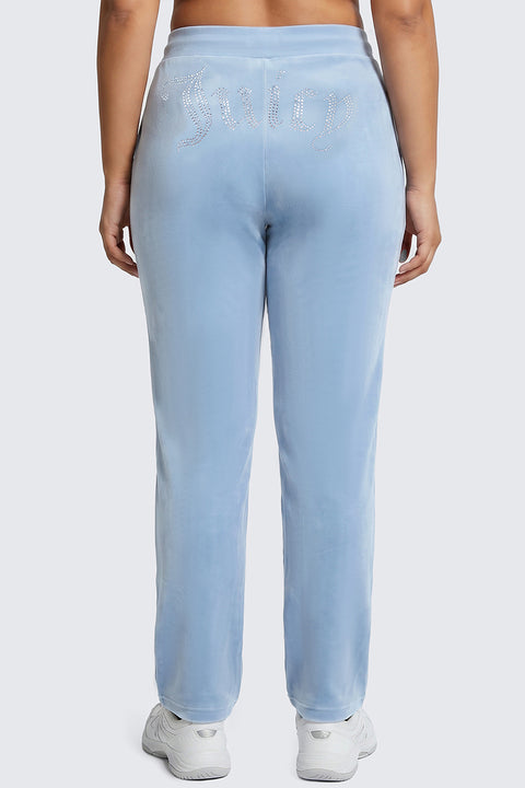 A person wearing the Plus-Size OG Big Bling Velour Track Pants in light blue, featuring a sparkling Juicy rhinestone embellishment on the back, stands facing away from the camera and channels iconic Y2K style.