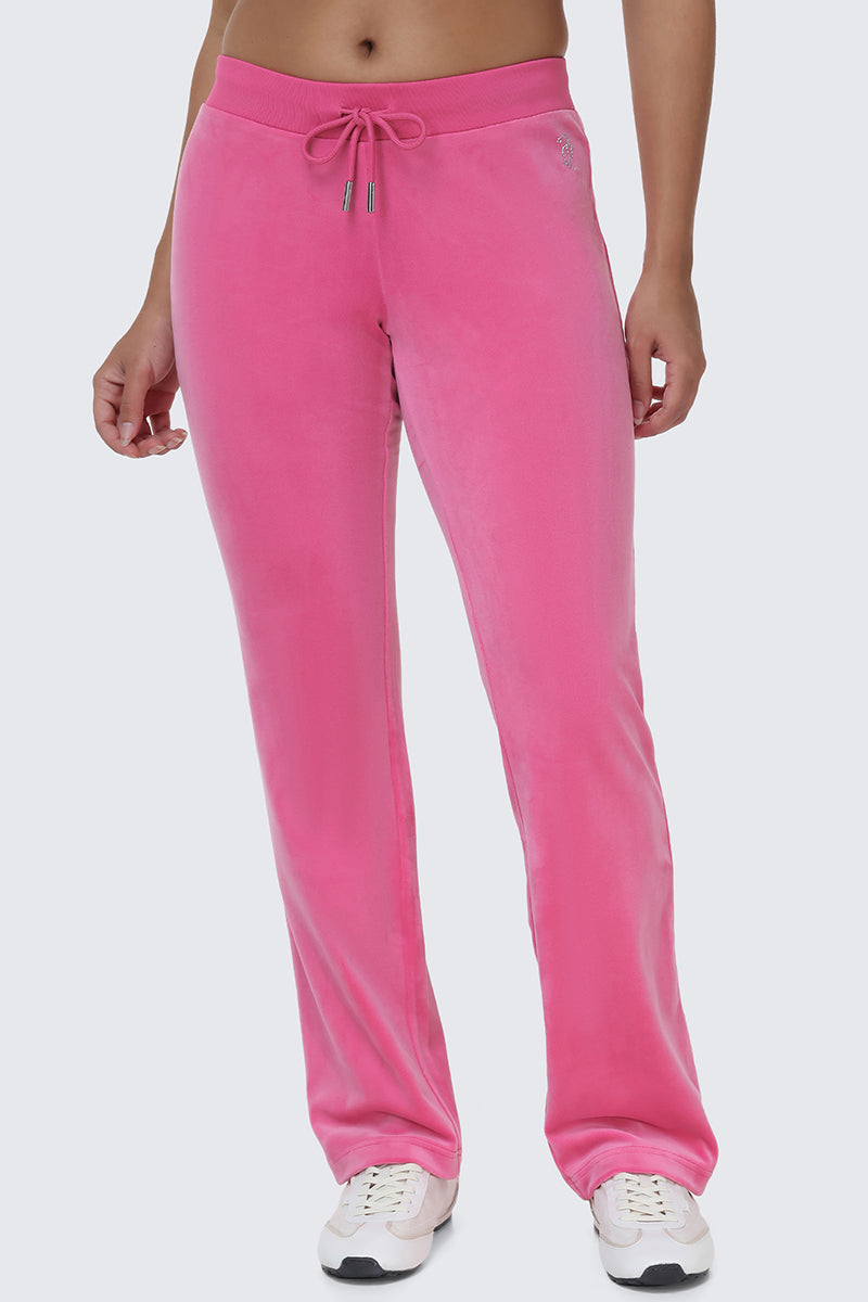 Wearing OG Big Bling Velour Track Pants in bright pink with a drawstring waist, paired with white sneakers, standing against a plain light background.