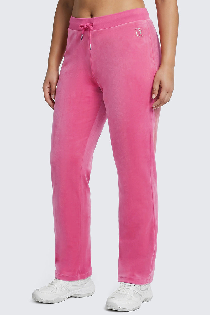 A person is shown from the waist down, wearing Plus-Size OG Big Bling Velour Track Pants in vibrant pink with a drawstring waist, paired with white sneakers. The plain light background and visible lower half channel serious Y2K energy.