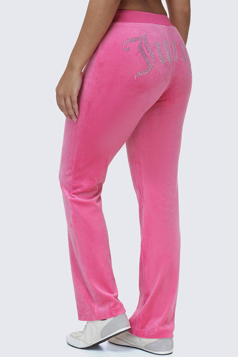 Wearing the OG Big Bling Velour Track Pants in vibrant pink, adorned with sparkling rhinestones that spell out Juicy across the back for an unmistakable Y2K flair, this person is photographed from behind—highlighting only their lower back and legs—styled with classic white shoes.