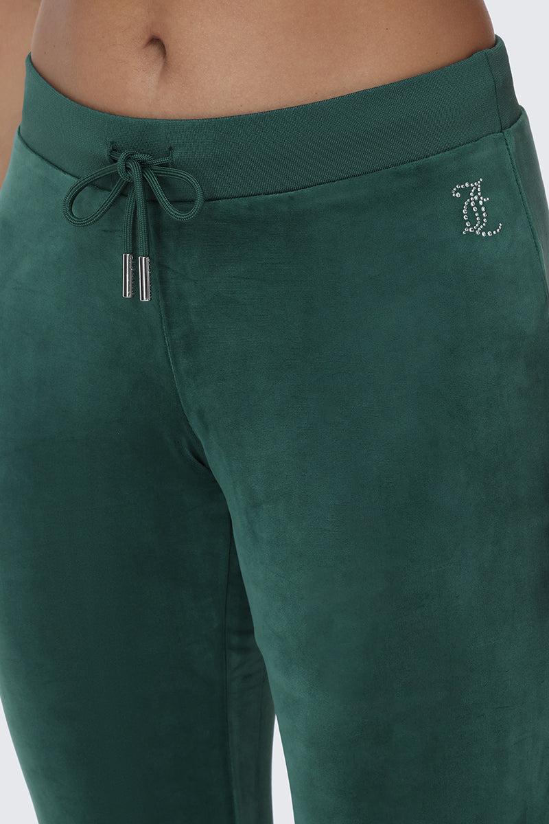 Close-up of a person wearing the OG Big Bling Velour Track Pants in dark green, featuring a drawstring waist and a rhinestone L logo on the left hip—a signature Juicy embellishment that defined Y2K fashion.