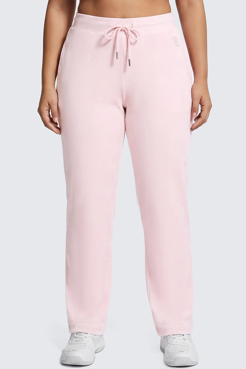 A person is wearing the Plus-Size OG Big Bling Velour Track Pants in light pink with a drawstring waist, standing against a plain background. These Juicy-inspired relaxed-fit sweatpants are styled with white sneakers for an effortlessly chic Y2K look.