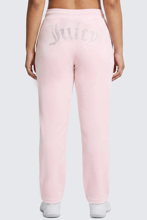A person is shown from behind wearing the Plus-Size OG Big Bling Velour Track Pants in light pink, featuring “Juicy” written in rhinestones across the back. The Y2K-inspired look is finished with a pair of crisp white sneakers.