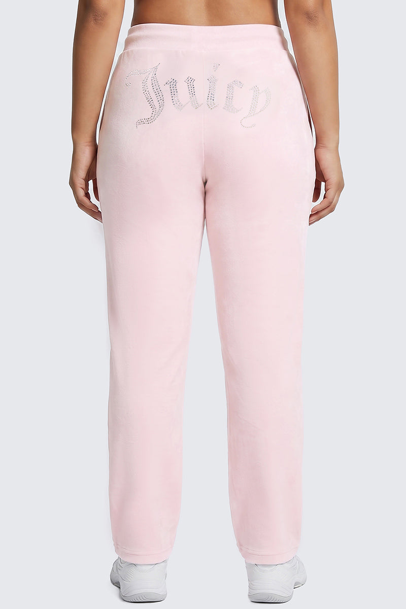 A person is shown from behind wearing the Plus-Size OG Big Bling Velour Track Pants in light pink, featuring “Juicy” written in rhinestones across the back. The Y2K-inspired look is finished with a pair of crisp white sneakers.