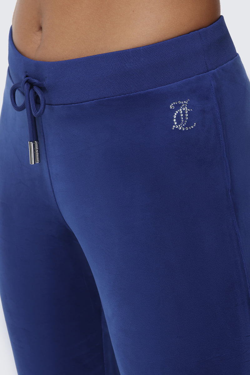 Close-up of a person wearing the OG Big Bling Velour Track Pants in royal blue, featuring a drawstring waist and a small rhinestone B logo on the hip for that signature Y2K vibe with sparkling Juicy embellishments.
