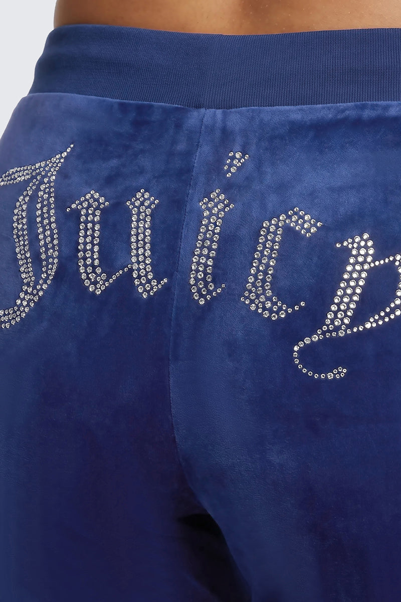 Close-up of a person wearing the Plus-Size OG Big Bling Velour Track Pants, featuring blue velour fabric and a sparkling rhinestone Juicy embellishment across the back—a true Y2K style statement.