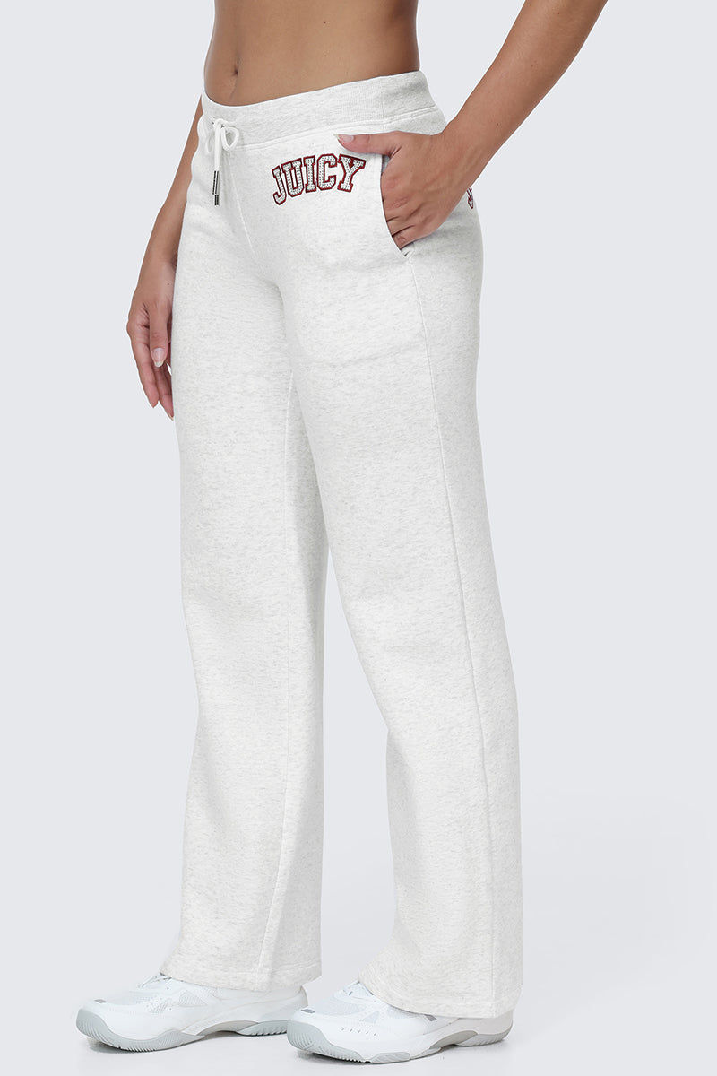 Wearing the Small Bling Fleece Wide Leg Pants—white, wide-leg fleece pants featuring a drawstring waistband and a sparkling red rhinestone Juicy logo on the left hip—paired with white sneakers and a cropped top, this person stands against a plain background with one hand in their pocket.